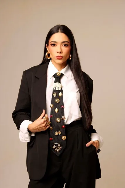 Mulher de terno preto, camisa branca e gravata estampada, em estúdio com fundo bege.