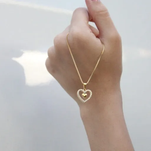 Mão segurando um colar dourado com pingente de coração.